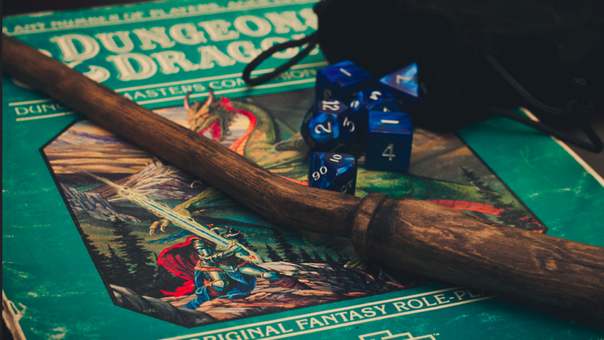 Wooden wand, blue polyhedral dice, and black velvet bag sitting on a teal "Dungeons and Dragons" player's manual