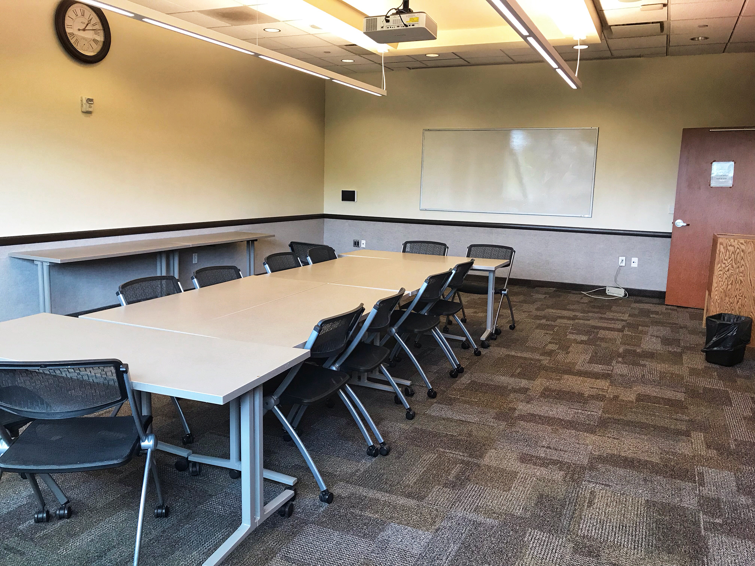 Upstairs Conference Room showing tables put together to resemble conference table, chairs, and white board mounted on wall