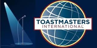 "Toastmasters International" logo, blue globe with latitude and longitude lines behind white rectangle, dark blue background with microphone and spotlight
