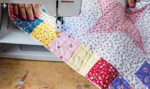sewing a quilt on a sewing machine, painted fingernails, blue, yellow, pink, and white patches